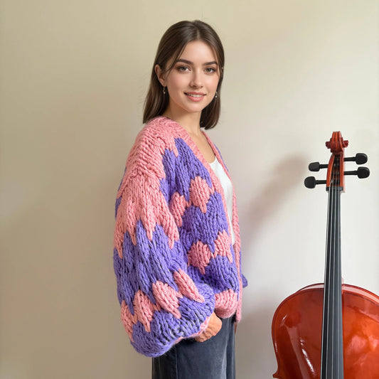 Woman in oversized pink and purple chunky knit cardigan by HazumiCrafts standing next to cello