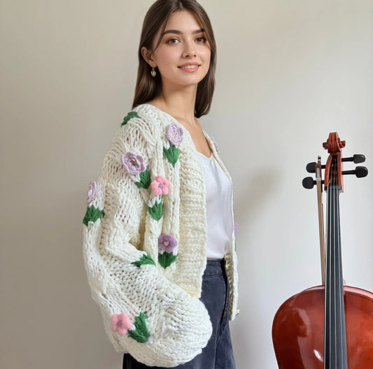 Woman in chunky knit floral cardigan and white top standing by a cello, HazumiCrafts knitwear