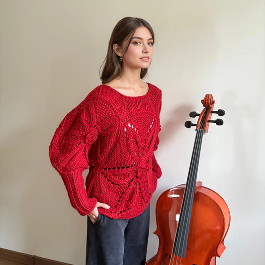 Woman in oversized red chunky knit sweater by HazumiCrafts standing beside a cello indoors