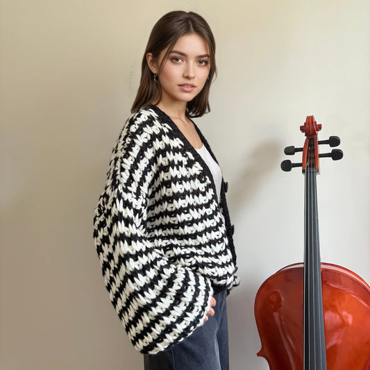 Woman in black and white chunky knit sweater by HazumiCrafts standing next to a cello